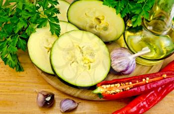 Zucchini, garlic, hot red pepper, a bottle of vegetable oil, parsley on a wooden board