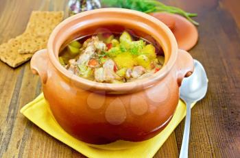 Roast with chicken and potatoes in a clay pot, a yellow napkin, spoon, crispbread, pepper in the pot on a board