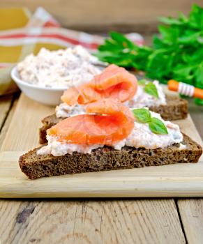 Toast two slices of rye bread with cream, basil and salmon, knife, napkin, parsley on a wooden boards background