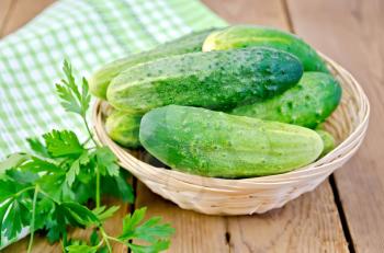 Cucumbers in a wicker basket, parsley, doily on a wooden boards background