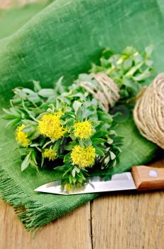Rhodiola rosea flowers tied with twine, ball of twine, knife on green napkin on a wooden board
