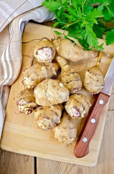 Whole tubers of Jerusalem artichoke with parsley, knife, napkin, on the background of wooden boards