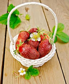 Ripe red strawberries with leaves and flowers in a white wicker basket on background wooden plank
