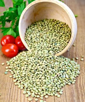 Green lentils in a wooden bowl with parsley and red tomatoes on a wooden boards background