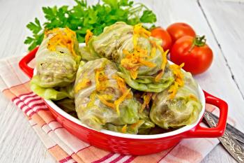Stuffed cabbage meat leaves with roasted carrots in a roasting pan on a red napkin, tomatoes, parsley on a lighter background board