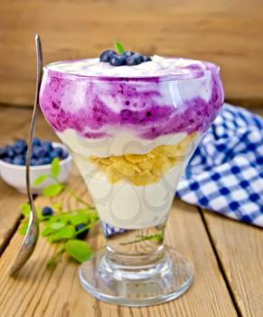 Milk dessert with blueberries, cereal and curd, spoon, napkin, blueberries on a wooden boards background