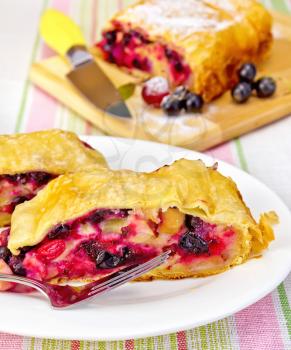 Strudel with black currant and cherry on a plate with fork, knife on background linen tablecloth