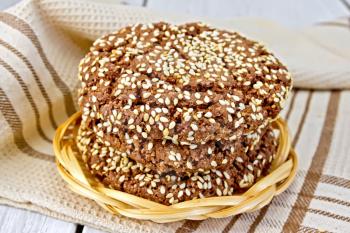 Chocolate cookies with sesame seeds in a wicker plate, napkin on a lighter background of the board