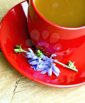 Chicory drink in a red cup with flower on a saucer on a wooden boards background from above