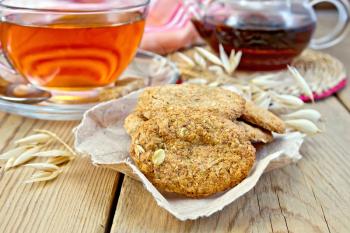 Oatmeal cookies with a stalk of oats on the paper, a cup of tea and teapot, napkin wooden boards background