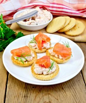 Round crackers with cream, dill and salmon in the plate, napkin, parsley on a wooden boards background