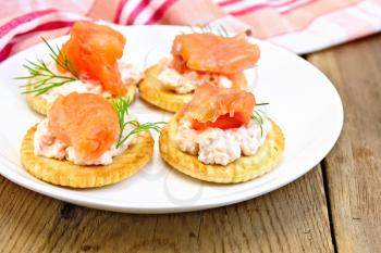 Round crackers with cream, dill and salmon in the plate, napkin on a wooden boards background
