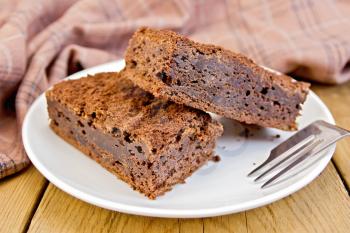 Two pieces of chocolate cake on a plate, fork, napkin on a wooden boards background