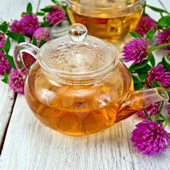Herbal tea with clover flowers in a glass teapot and cup on the background light wooden boards