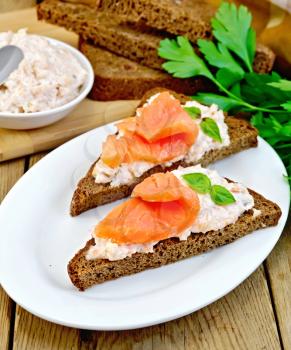 Sandwiches on two triangular pieces of rye bread with cream, basil and salmon, knife, napkin, parsley on a wooden boards background