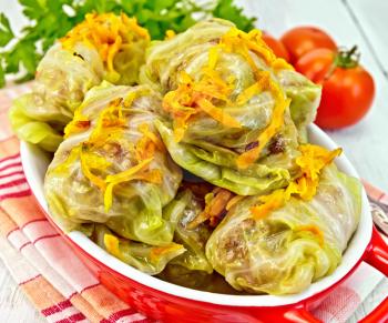 Stuffed cabbage meat in cabbage leaves with roasted carrots in a roasting pan on a red napkin, tomatoes with parsley on a light background boards