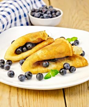 Two pancakes with blueberries and mint on a white plate, napkin, bowl with berries on a wooden boards background