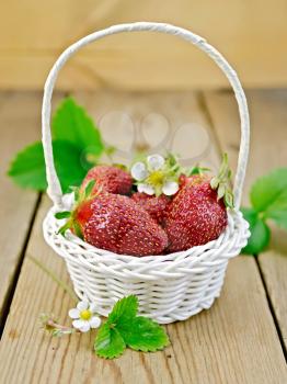 Ripe red strawberries with flowers and green leaves in a white wicker basket on a wooden boards background