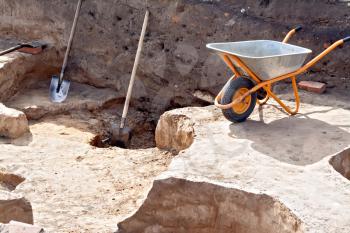 Shovel, wheelbarrow at the site Archaeological excavations on a background of brown soil