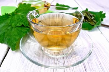 Herbal tea in a glass cup with saucer and teapot, sage leaves on the background light wooden boards