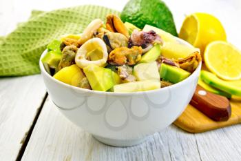 Salad from shrimps, octopus, mussels and calamari with avocado, lettuce, lemon and pineapple in a bowl, green cloth on a background of light wooden boards