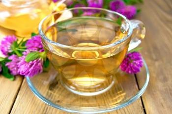 Herbal tea with flowers of clover in a glass cup and teapot on a wooden boards background