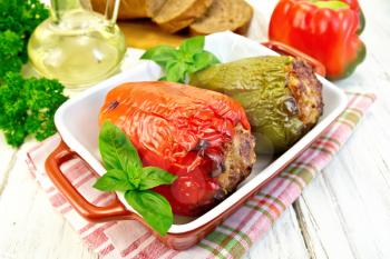 Two sweet peppers stuffed with meat and rice with basil leaves in a brown roasting pan on a napkin, parsley, bread on a wooden boards background