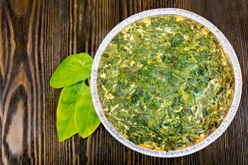 Celtic cake with spinach, tomatoes, oatmeal and eggs in baking dish from a foil, spinach leaves on the background of wooden boards on top