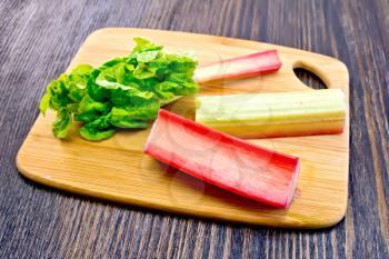 The stalks of rhubarb with green leaf on the planch on a dark wooden board