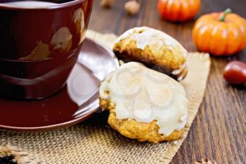 Pumpkin Cookies with a brown cup on a napkin of burlap, pumpkin, acorn on a wooden boards background