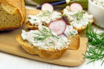 Bread with pate of cottage cheese, dill and radish on a wooden board, a napkin on background wooden table