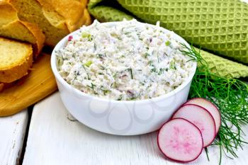 Pate of cottage cheese, dill and radish in a bowl, radish slices, dill, bread and a napkin on a wooden boards background