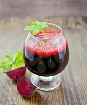 The juice of beet in wineglass,  beet slices and parsley on a dark wooden board