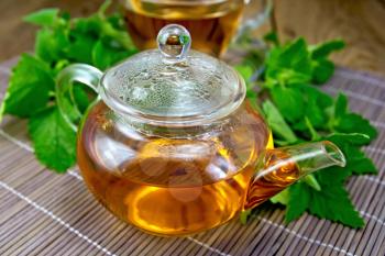 Herbal tea in a glass teapot of fresh mint leaves on bamboo napkin background and wooden board