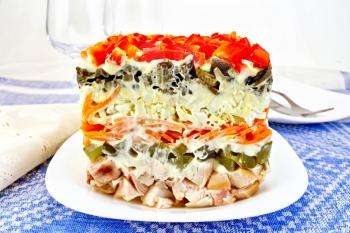 Layered salad with chicken, egg, mushrooms and cucumber, carrots and pepper, mayonnaise on the background of the tablecloth