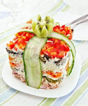 Layered salad with chicken, egg, mushrooms and cucumber, carrots and pepper, mayonnaise on the plate against the background of napkin