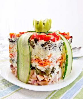 Layered salad with chicken, egg, mushrooms and cucumber, carrots and pepper, mayonnaise on the plate against the background of striped napkins