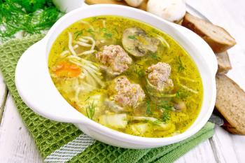 Soup with meatballs, noodles and mushrooms in a white bowl on a green napkin, parsley on a wooden boards background