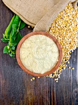 Flour pea in a clay bowl, flakes in a bag and fresh pods on a background of wooden boards on top