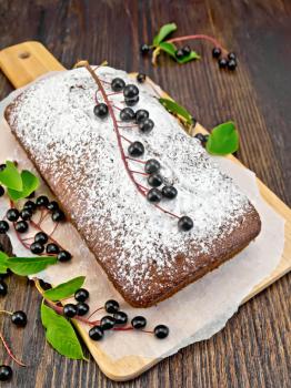 Fruitcake bird cherry with berries on a paper on the background of the wooden board