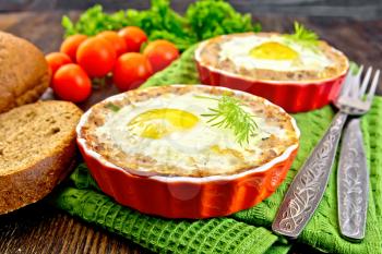 Two forms of tartlets with meat and eggs in the forms on a napkin, tomatoes, bread, parsley and dill on background of wood planks