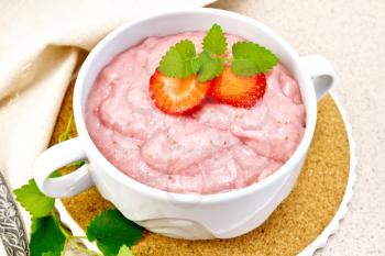 Strawberry soup with berries and mint in a bowl on a stand, a towel and a spoon on a background of a granite table
