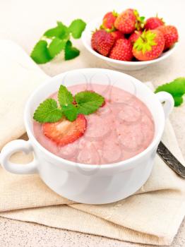 Strawberry soup with berries and mint in a bowl on a towel, spoon on a background of a granite table