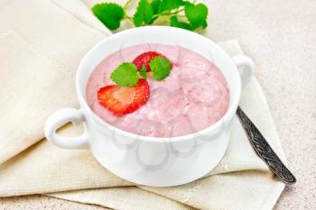 Strawberry soup with berries and mint in a bowl on a napkin, spoon on a background of a granite table