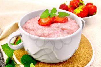 Strawberry soup with berries and mint in a bowl on a stand, a towel on the background of the stone table