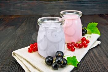 Milkshake with black and red currant in glass jars on a napkin with berries on a wooden board background