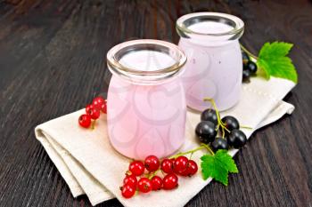 Milk cocktail with red and black currant in glass jars on a towel with berries on a wooden board background