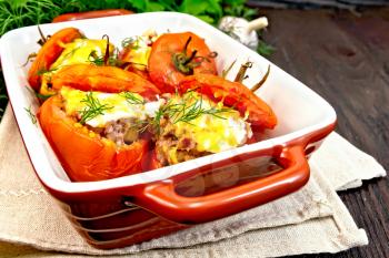 Tomatoes stuffed with meat and rice with cheese in a brazier on a towel, parsley, dill and garlic on a background of a dark wooden board