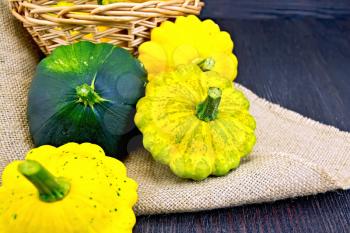Yellow and green squash on sackcloth and wicker basket on the background of dark wood planks