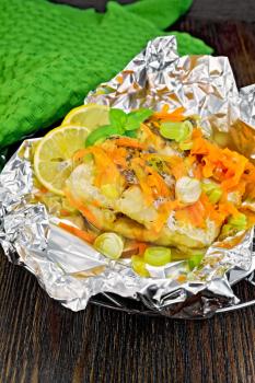 Pike with carrots, leek, basil and slices of lemon in foil on the lattice, a green towel on a dark wooden board